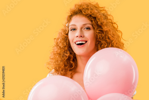 attractive smiling girl with pink balloons isolated on yellow © LIGHTFIELD STUDIOS