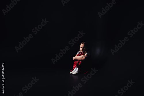 scared, lonely child sitting on floor on black background with copy space