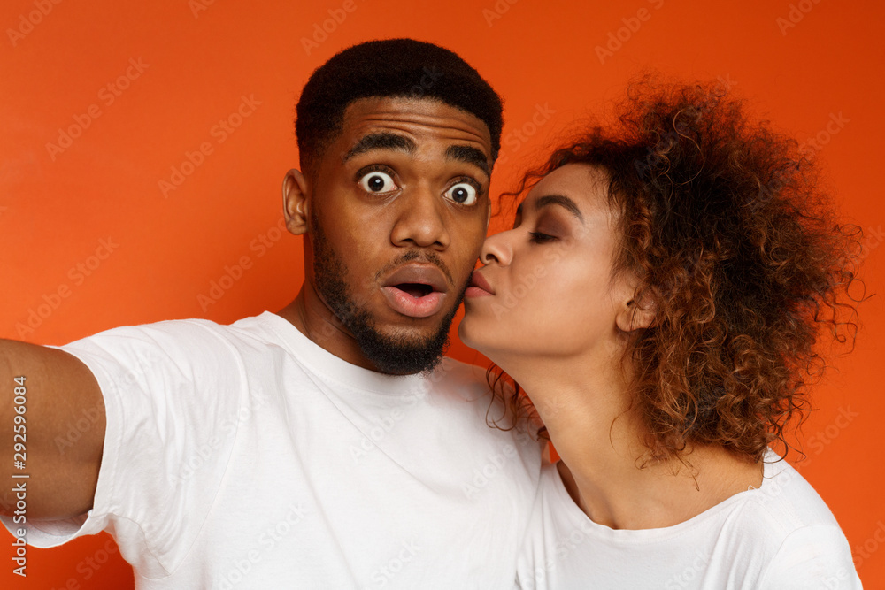 Shocked african guy taking selfie, woman kissing his cheek Shocked african guy taking selfie, woman kissing his cheek