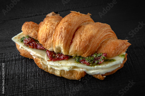 Vegetarian Croissant sandwich with mozzarella cheese, chedar, sun-dried tomatoes, pesto sauce. Healthy, tasty, nourishing snack. Take away food photo