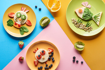 top view of plates with fancy animals made of food for childrens breakfast on blue, yellow and pink background