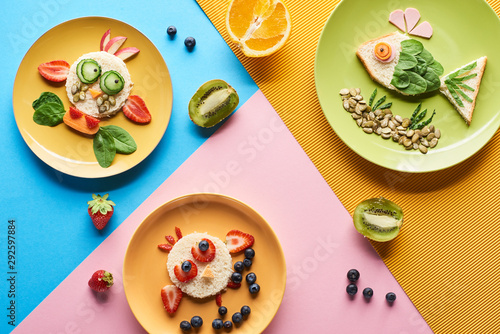 top view of plates with fancy animals made of food for childrens breakfast on blue, yellow and pink background