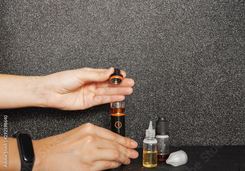 Popular vape device and liquids. No smoking. Change habit of smoking. Concept for more healthy life. Flat lay of bad habits on black sparkling backdrop. E-cigarette kit. Hand opening vape