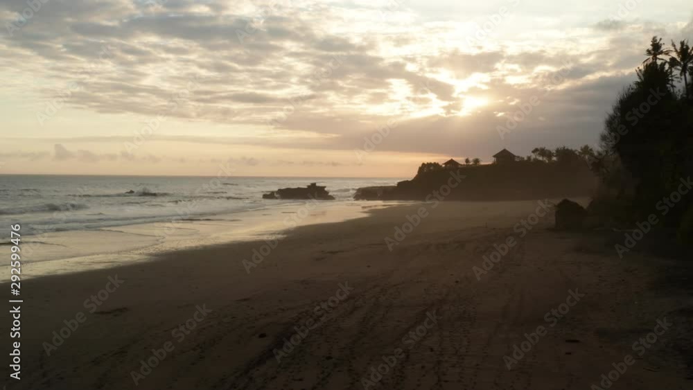 Aerial view looking down onto a tropical beach at sunset in mist with large ocean waves rolling in Bali, Indonesia Aerial view looking down onto a tropical beach at sunset in mist with large ocean waves rolling in Bali, Indonesia