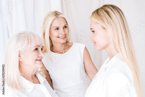 elegant three-generation blonde women in total white outfits looking at each other