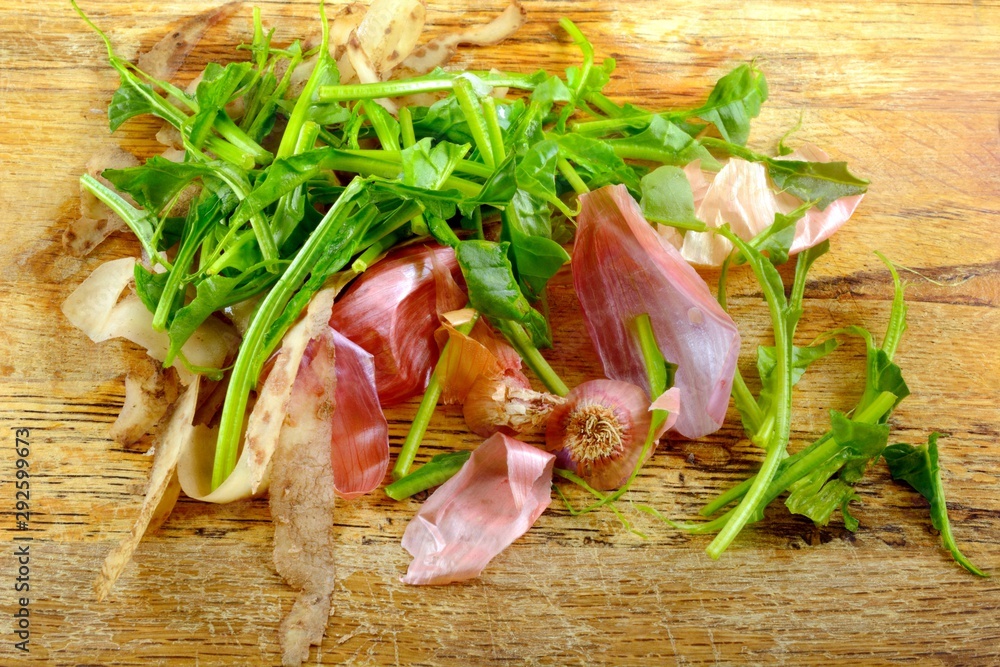 Food waste after meal preparation of spinach stalks, onion skin and potato peels on wooden cutting board