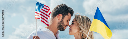 panoramic shot of attractive woman and handsome man smiling and holding american and ukrainian flags