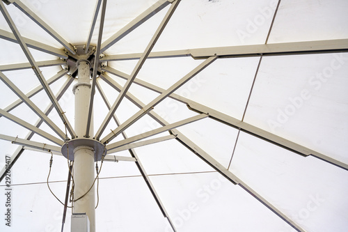Fototapeta Naklejka Na Ścianę i Meble -  Large market or gastronomy parasol with white fabric and metal struts, which are opened by motor drives, seen from below, background texture