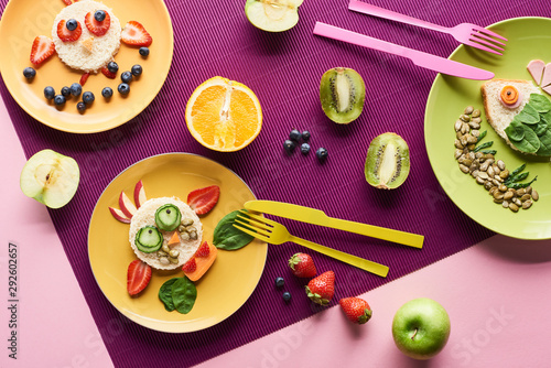 top view of plates with fancy animals made of food near fruits on purple background