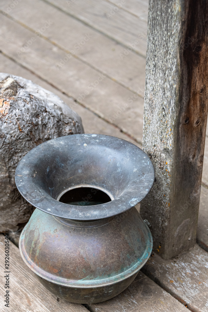 Antique copper spittoon on wood deck next to weathered wood post Antique copper spittoon on wood deck next to weathered wood post