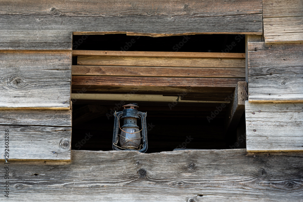 Close up of outside wall of rustic wood building, open window with dusty lantern on windowsill