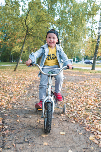 little boy, child 3-5 years old, smiles happy, laughs, rides bicycle, on summer spring autumn day in a city park, keeps his balance, rests on weekends, learns to ride bicycle training and dexterity. © byswat