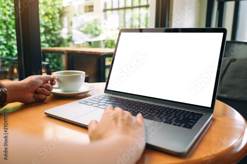 Mockup image of a woman using and touching laptop touchpad with blank white desktop screen while drinking coffee