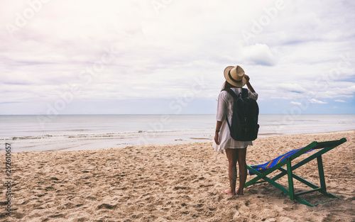 A female traveler with hat and backpack standing alone on the beach by the sea