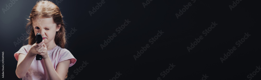 panoramic shot of kid holding pistol while looking at camera on black background panoramic shot of kid holding pistol while looking at camera on black background