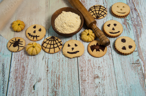 Homemade cakes for Halloween. Cornmeal, rolling pin, baking paper, cookies with spiders, bats, pumpkins, scary smiles, cobwebs on a light blue wooden background.