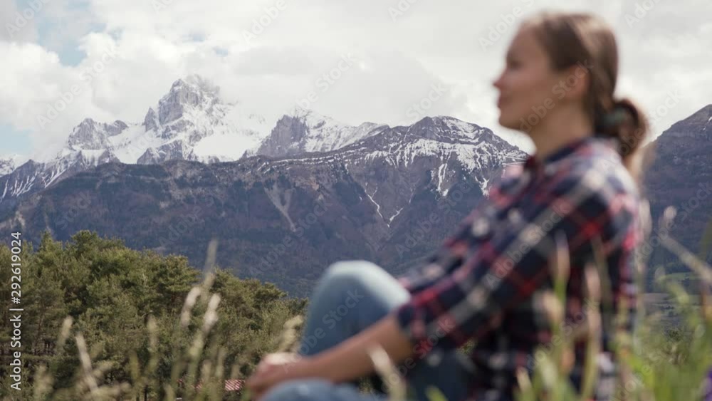 Picturesque view of Alps mountains and blurred image of tourist woman sitting on a green meadow. Travel in Alps mountains Picturesque view of Alps mountains and blurred image of tourist woman sitting on a green meadow. Travel in Alps mountains