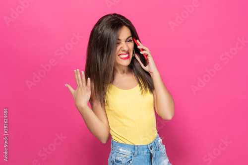 Nervous brunette talking on a cell phone and screaming into a phone on a pink background photo