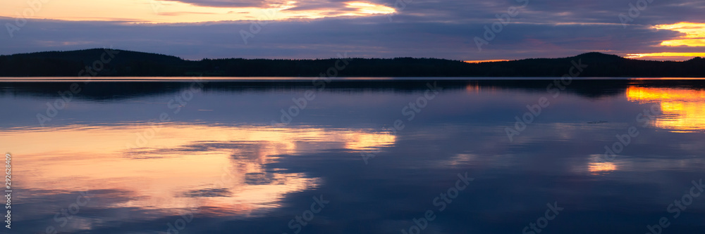Fototapeta premium Water reflections at midnight sun at serene lake in finlandd