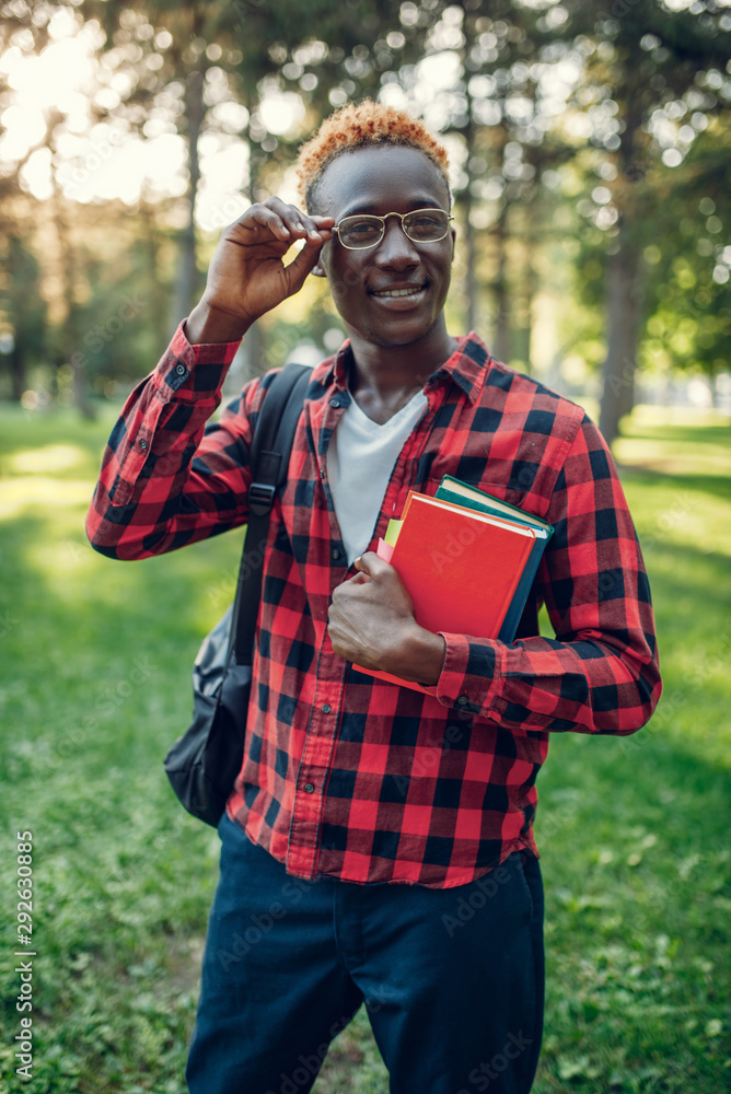 Obraz premium Black student in glasses holds book, summer park