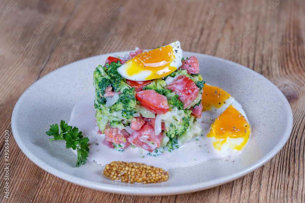 Delicious salad with broccoli, tomato, onion and boiled egg with cream sauce in plate on wooden background. Healthy food Delicious salad with broccoli, tomato, onion and boiled egg with cream sauce in plate on wooden background. Healthy food