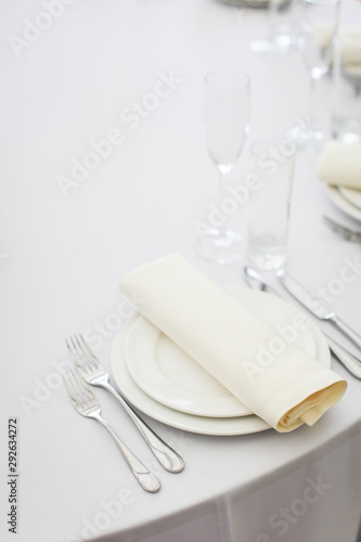 empty table served by white tablecloths  white plates  cutlery and glasses ready to receive guests in selective focus