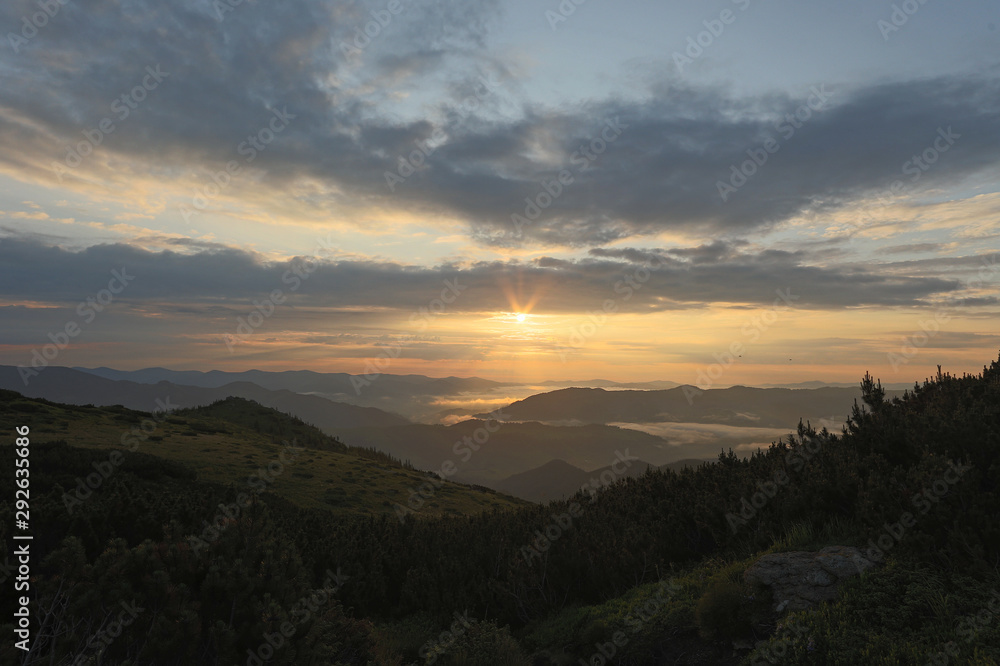 Fototapeta premium the top a mountain landscape under the rays of the rising sun, the light that illuminates the peaks of the mountain range of the valley covered with a gentle milky fog