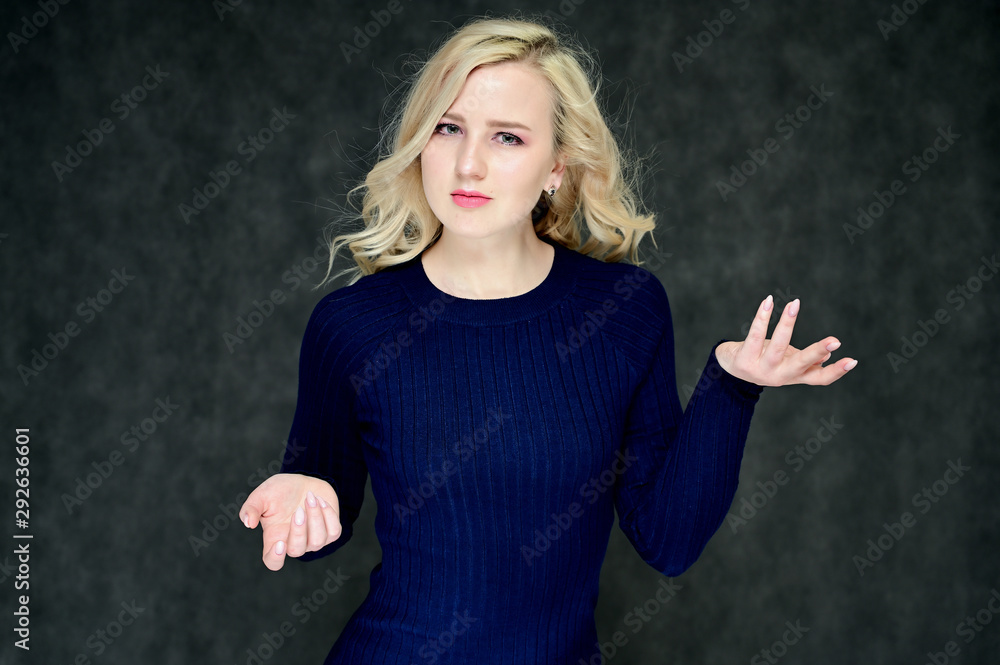 Portrait of a pretty young slim blonde girl with beautiful fluttering hair, great makeup, in a dark blue dress on a dark background. Made in the studio. Portrait of a pretty young slim blonde girl with beautiful fluttering hair, great makeup, in a dark blue dress on a dark background. Made in the studio.