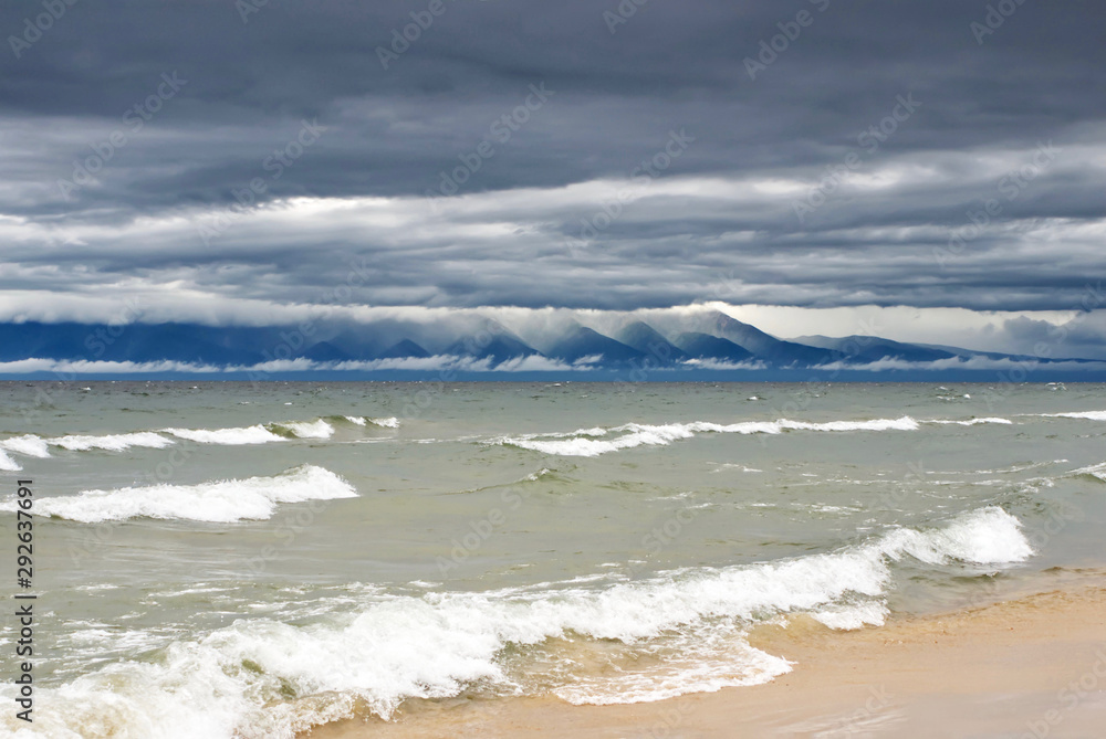The waves on the lake and thunderstorm clouds lie on the tops of the mountains on the horizon, Baikal lake Russia