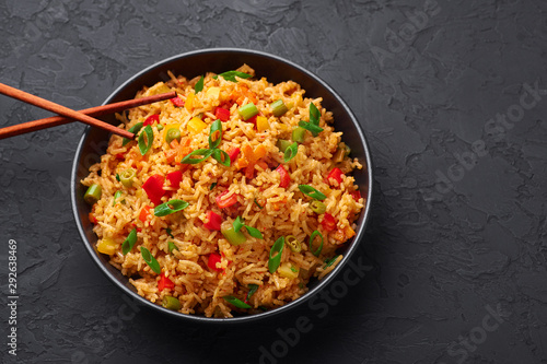 Veg Schezwan Fried Rice in black bowl at dark slate background. Vegetarian Szechuan Rice is indo-chinese cuisine dish with bell peppers, green beans, carrot. Copy space. Top view