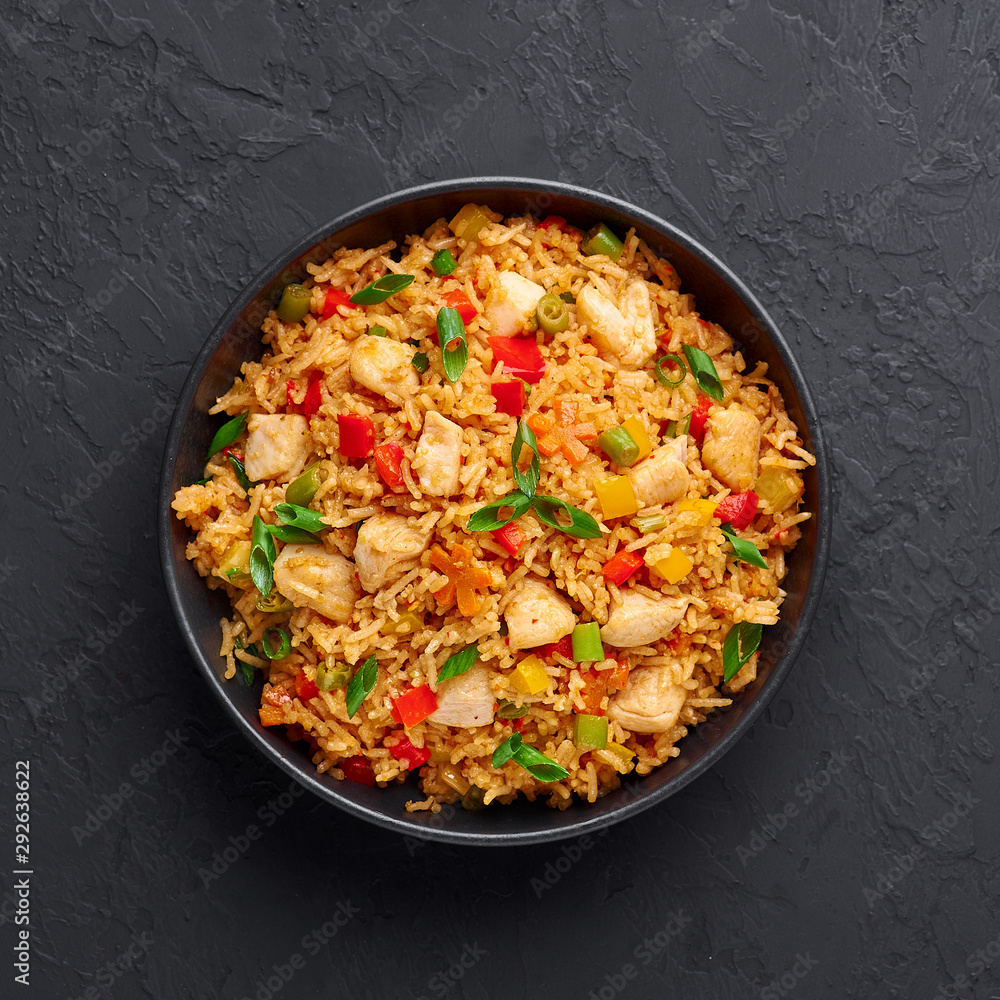 Schezwan Chicken Fried Rice in black bowl at dark slate background. Szechuan Rice is indo-chinese cuisine dish with bell peppers, green beans, carrot, chicken breasts. Copy space. Top view Schezwan Chicken Fried Rice in black bowl at dark slate background. Szechuan Rice is indo-chinese cuisine dish with bell peppers, green beans, carrot, chicken breasts. Copy space. Top view