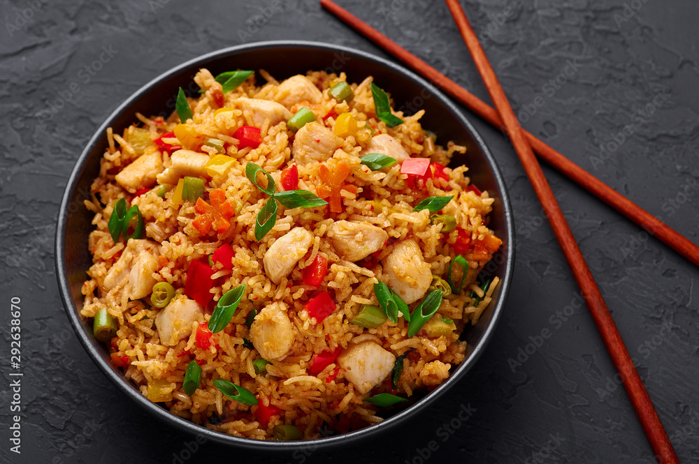 Schezwan Chicken Fried Rice in black bowl at dark slate background. Szechuan Rice is indo-chinese cuisine dish with bell peppers, green beans, carrot, chicken breasts. Schezwan Chicken Fried Rice in black bowl at dark slate background. Szechuan Rice is indo-chinese cuisine dish with bell peppers, green beans, carrot, chicken breasts.