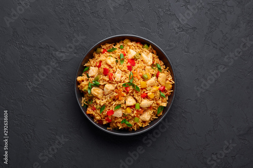 Schezwan Chicken Fried Rice in black bowl at dark slate background. Szechuan Rice is indo-chinese cuisine dish with bell peppers, green beans, carrot, chicken breasts. Copy space. Top view