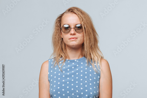Portrait of a girl in round glasses and a blue dress on a light gray background