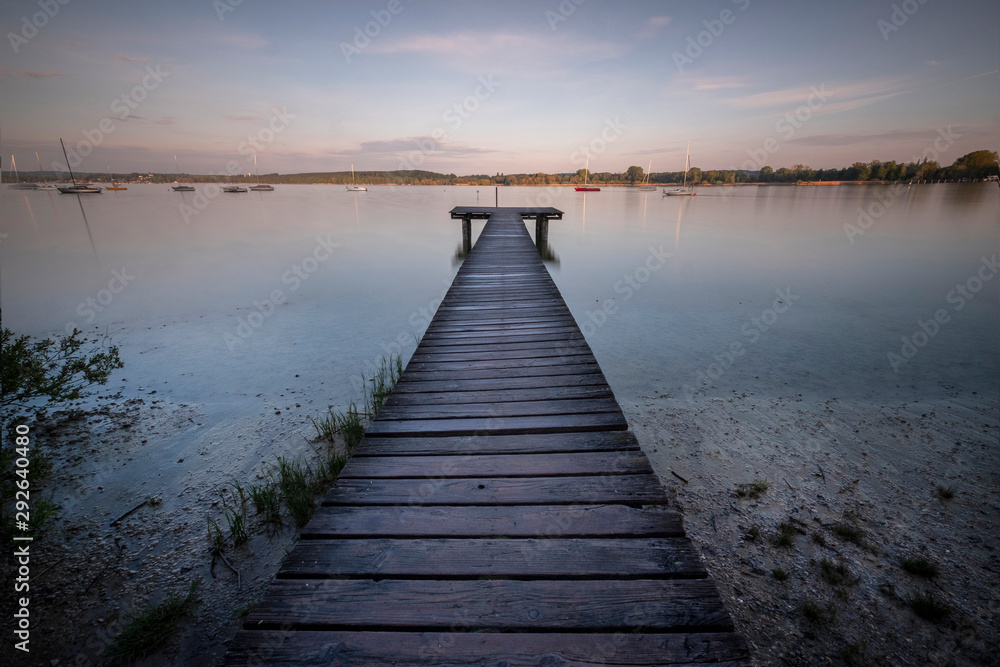 Small wooden bridge with a person meditating in the background on an Ammersee lake in Bavaria