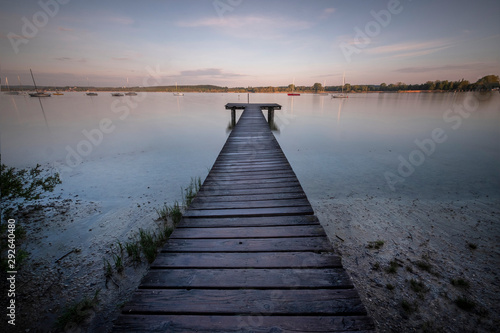 Small wooden bridge with a person meditating in the background on an Ammersee lake in Bavaria