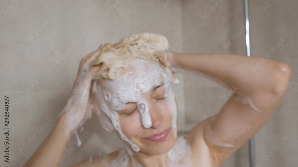 Stock Mature woman taking shower washing her hair in hot water in bathroom. Woman enjoying taking a shower cleaning her face and rinsing her body at home. | Adobe Stock
