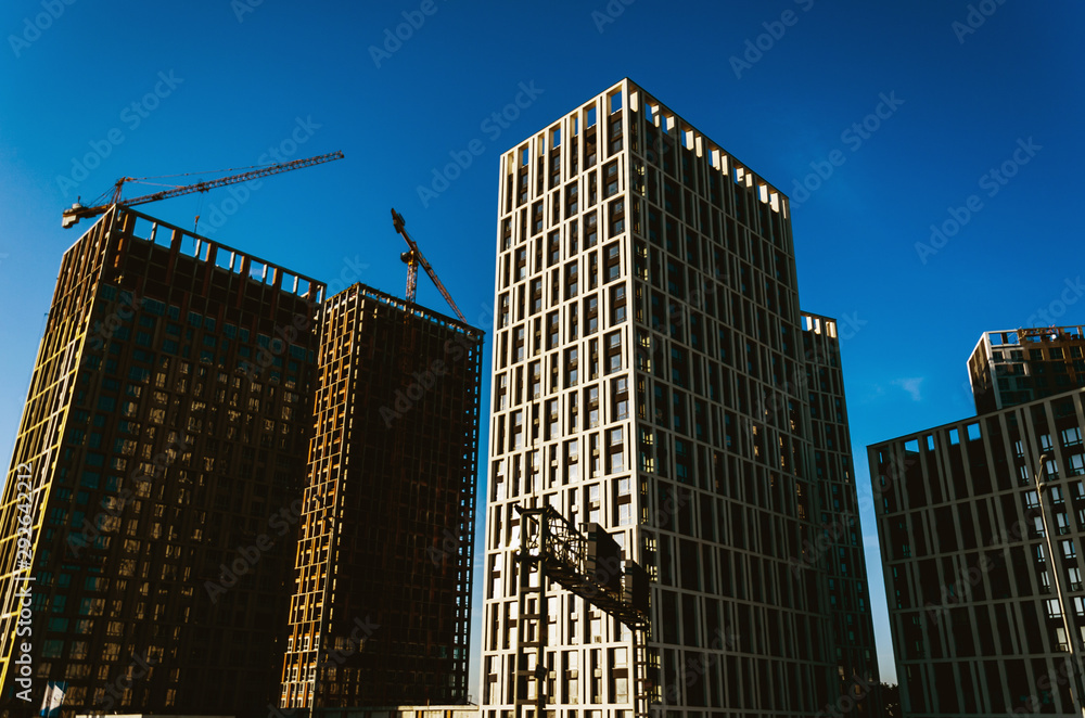 Housing development. Modern high-rise buildings under construction and cranes against a clear blue sky. Urban background. Urban sprawl concept