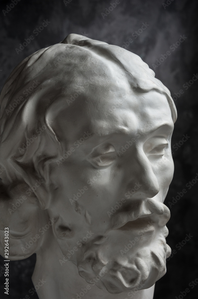 Gypsum copy of ancient statue John the Baptist head on dark textured background. Plaster sculpture man face.
