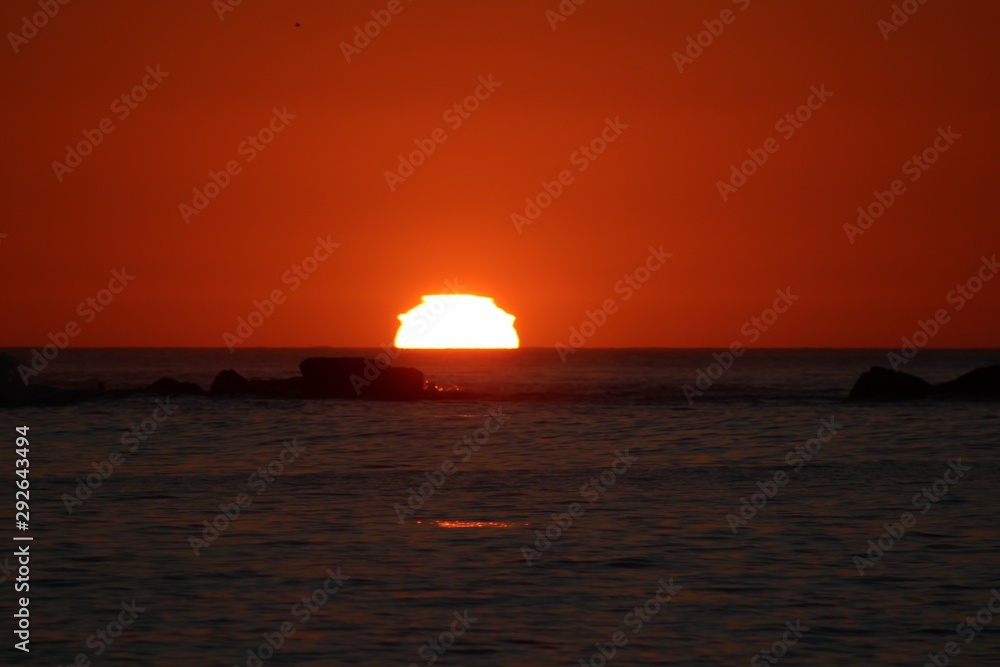 sun reaching the horizon in the sea on a red sky sunset