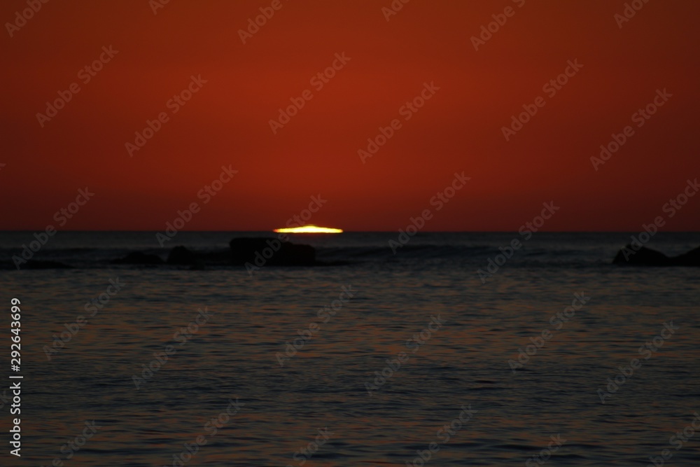 sun reaching the horizon in the sea on a red sky sunset