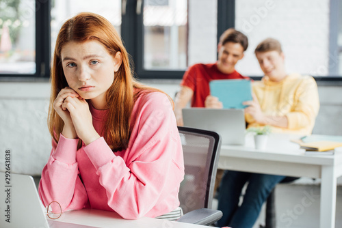 sad pensive girl and classmates laughing at her in school