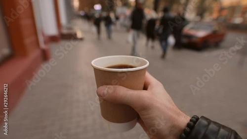 1st person view, man holding and carries paper coffee cup walking along city street
