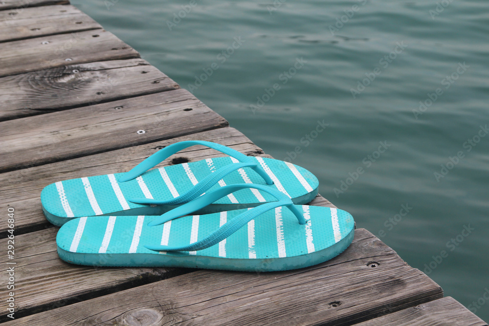 Naklejka premium Flip flops at the wooden pier at lake 