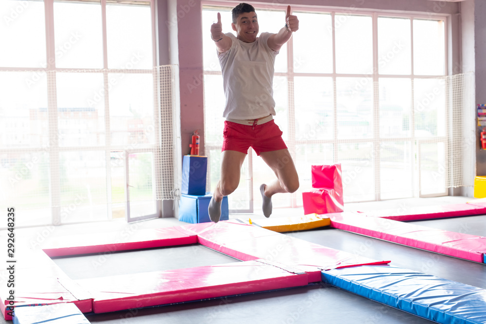 Fototapeta premium Fitness, fun, leisure and sport activity concept - Handsome happy man jumping on a trampoline indoors