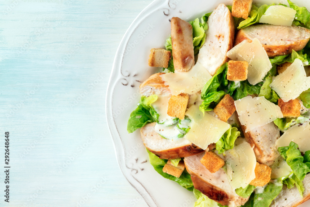 Caesar salad close-up. Slices of chicken breast, green lettuce, Parmesan cheese, and croutons, overhead shot with copy space
