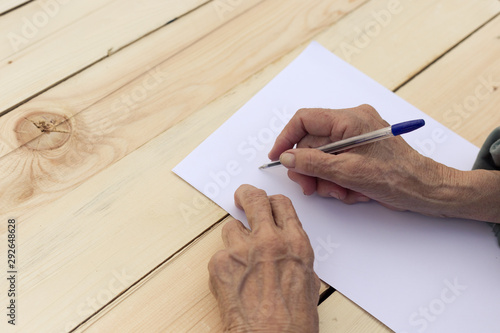 Hands of an elderly man are holding blank paper and a pen. Concept of testament, signing of an agreement, writing in old age. Image.