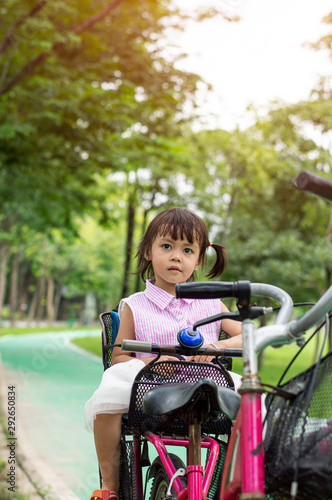 Asian children girl sit behind the bicycle rider in park.
