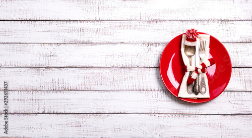 Christmas table setting with holiday decorations in the form of a knitted hat and scarf in white and red on an old wooden background with copy space.