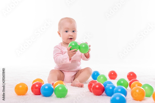 Small baby girl on a white carpet in a light room.